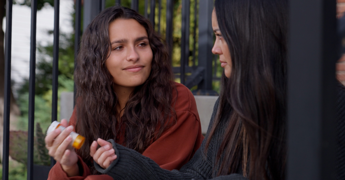 one woman holding a prescription bottle of medicine and talking to another woman